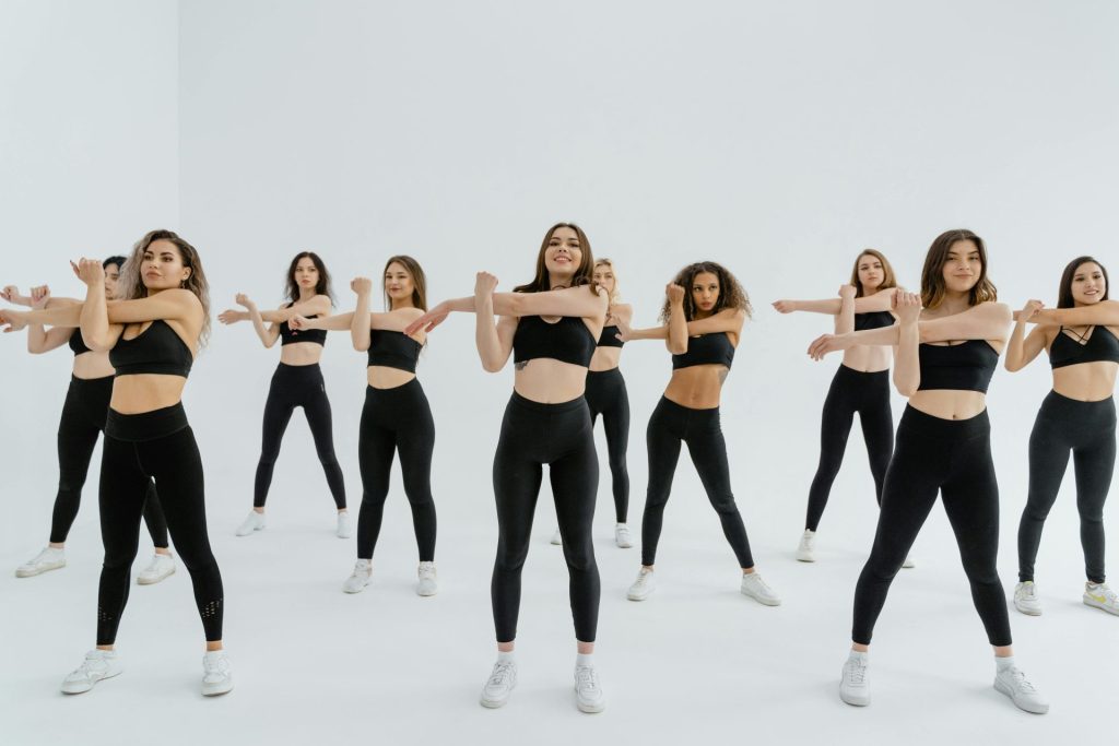 A group of women in athletic wear performing exercises in a studio with a white background.